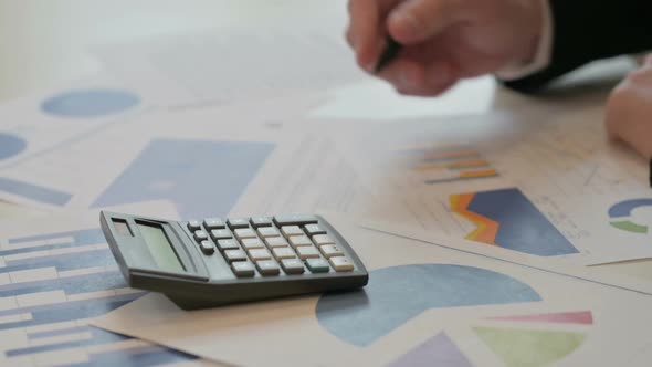 Close Up of Middle Aged Businessman Writing on Paper Using Calculator