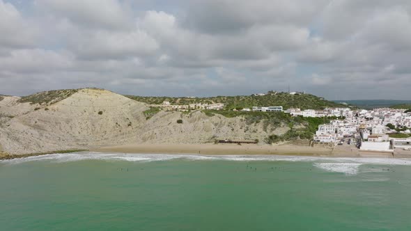 Aerial shot approaching surfers waiting for waves along the beach of a picturesque coastal town with