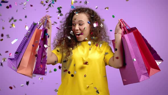 Excited Woman with Colorful Paper Bags After Shopping Screaming During Confetti Rain in Violet