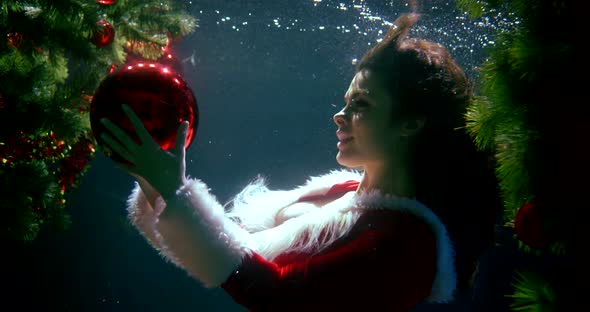 Beautiful Cheerful Girl in a Christmas Red Suit, She Is Under Water, Next To Her Two Christmas Trees