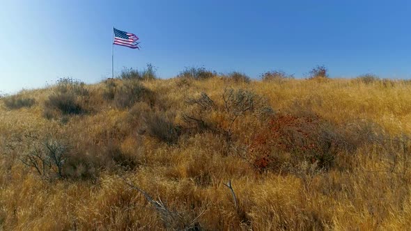 American Flag Fluttering in the Wind Above the Dry Bushy Hill