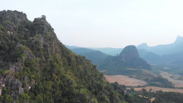 Aerial: flying over rice paddies unique valley scenic cliffs rock pinnacles tropical jungle Laos