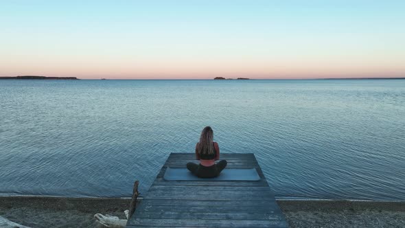 The tanned girl does yoga and meditation on the mat near the sea. Morning, dawn. Aerial view