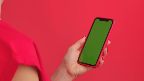 Female Hand Holds Mobile Phone with Green Workspace Mock Up Screen on Red Studio Background in