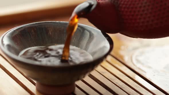 Tea is Poured Into a Bowl From a Red Chinese Teapot