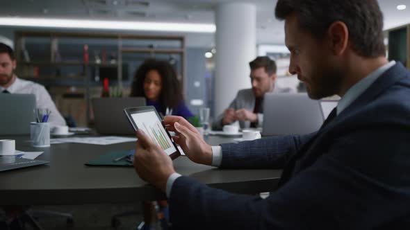 Serious Businessman Searching Tablet Looking Graph Charts on Corporate Meeting