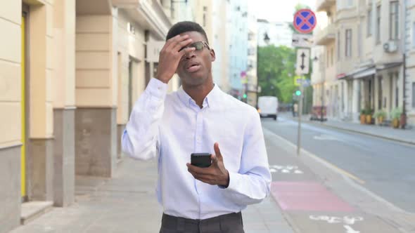 African Man Reacting to Loss on Smartphone While Walking on the Street