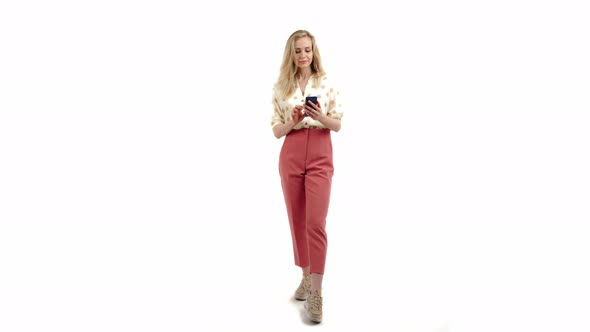 Nice Caucasian Blonde Girl Looking Into the Phone Wearing Shirt and Pink Trousers Full Shot White