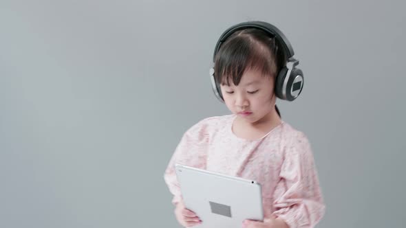 Little Asian girl with headphone enjoy watching video online on tablet and dancing happily.