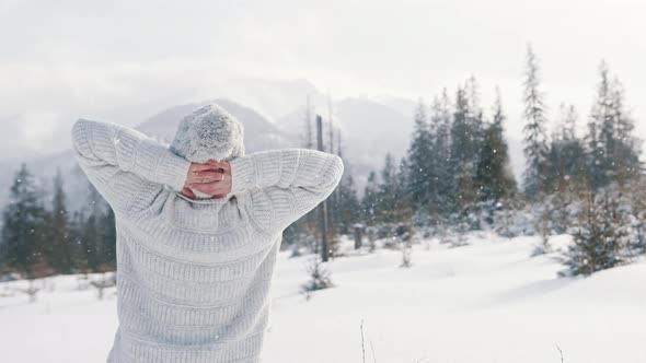 Young Woman in White Sweater and Woolen Hat Enjoying Mountain Landscape and Snowfall