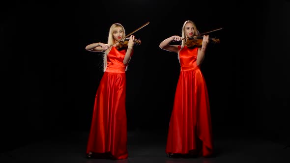 Two Girls Blonde Playing the Fiddle. Studio. Black Background