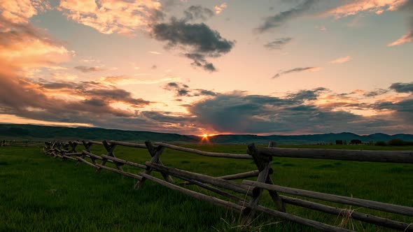 Time lapse of colorful sunset along wood fence in pasture