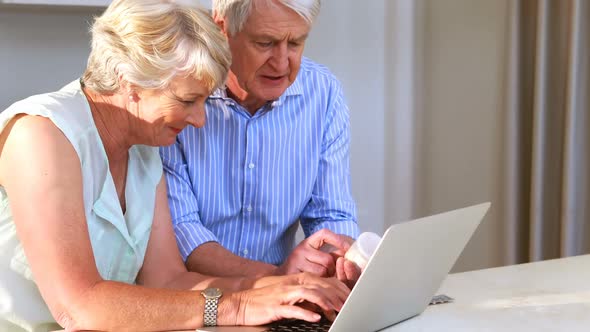 Senior couple checking medicine while using laptop in kitchen