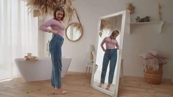 Pretty Happy Female Showing Her Weight Loss By Wearing Old Jeans Indoors