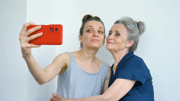 Adult Daughter and Senior Mum are Taking Selfportrait Picture Selfie on Red Smartphone Together