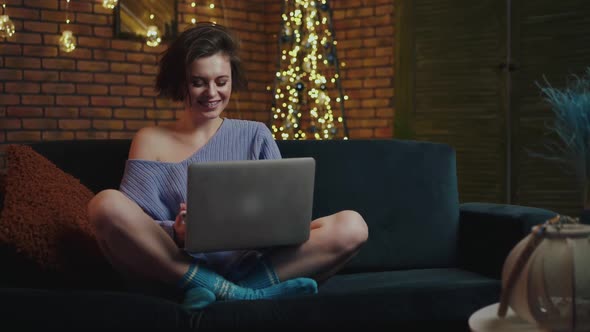 Girl with Smile on Face Uses Laptop During Relaxing on Cozy Sofa in Home