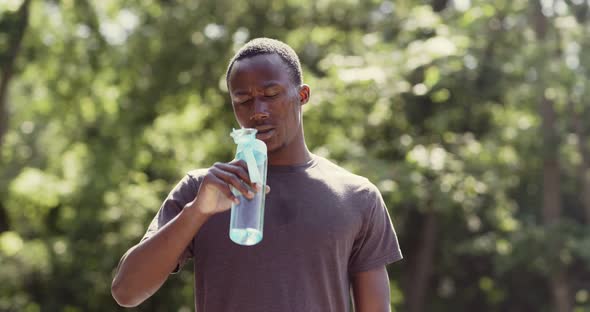 Overheated African American Guy Drinking Water From Bottle in Park