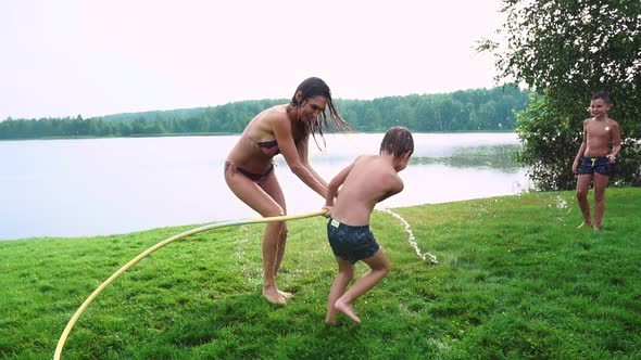 Mom Dad and Two Sons in the Summer on the Grass Poured Water From a Hose for the Lawn. Area Country