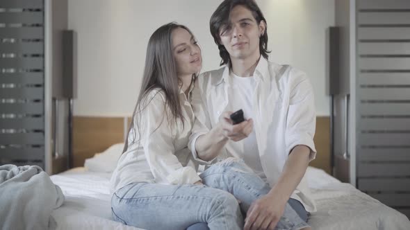 Portrait of Young Couple Watching TV at Home in Bedroom. Happy Relaxed Caucasian Man and Woman