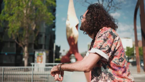 Confident curly-haired bearded man in eyeglasses correcting his hairstyle