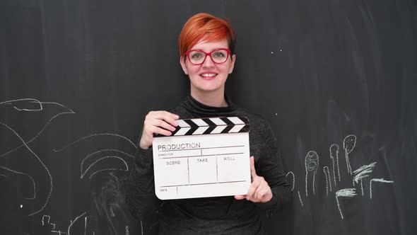 Redhair Woman Actress Posing with Movie Clapper Board Smiling and Looking at Camera Against