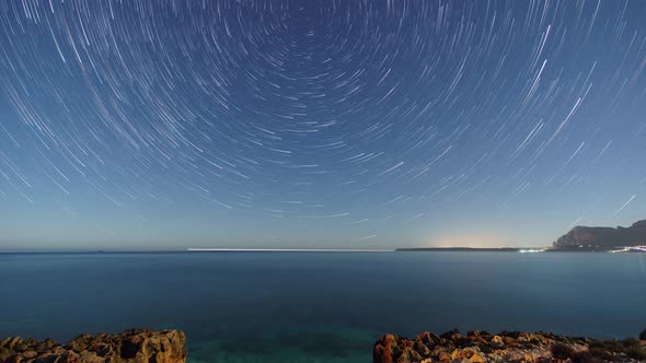 Startrails around polaris over rocky coastline of mediterranean sea with clear turquoise water at na