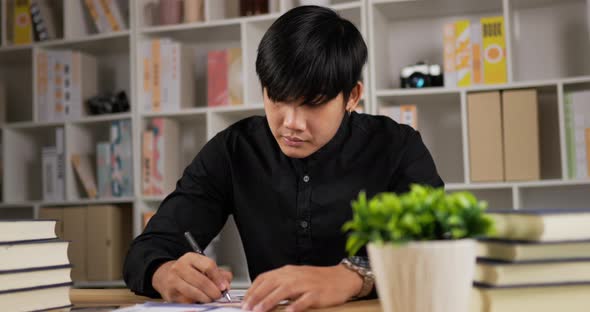 Focused young asian worker man writing paperwork at home