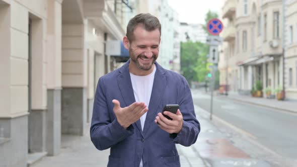 Man Celebrating Success on Phone While Walking Down the Street