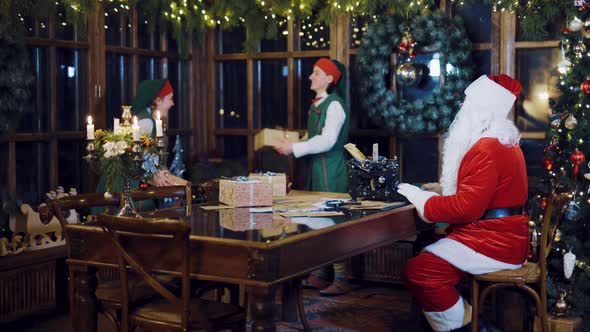Santa Claus is Writing a Letter on the Typewriter and Watching Elves 