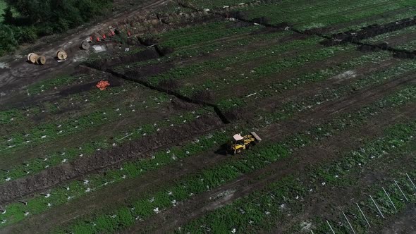 Aerial View of Massive Field with an Excavator Driving in Between Rows of Racks