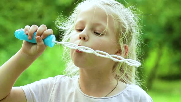 Portrait of funny lovely little girl blowing soap bubbles. Happy carefree childhood.