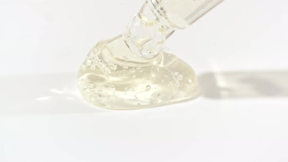Macro Shot of Transparent Yellow Cosmetic Fluid Gel Cream With Bubbles in Pipette Drips on a White