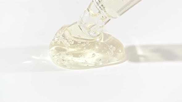 Macro Shot of Transparent Yellow Cosmetic Fluid Gel Cream With Bubbles in Pipette Drips on a White alt