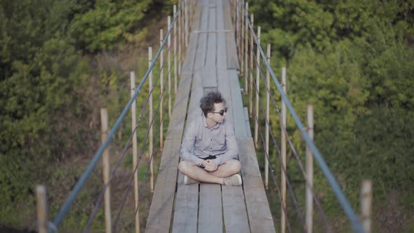 Guy Walks on Suspended Bridge in the Forest