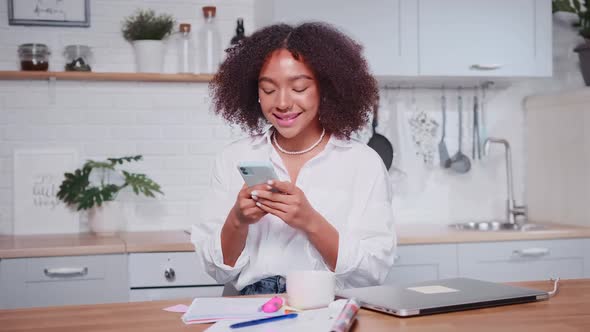Young African American Woman Writes Messages on Phone and Smiles