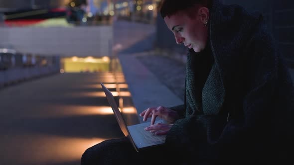 Young woman with blanket using laptop in the city at night