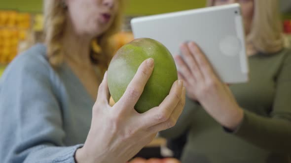 Close-up of Female Caucasian Hand Holding Pomelo As Blurred Women Using Tablet at the Background