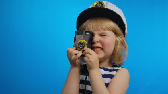 Little Girl in a Sailor Dress is Using Retro Photo Camera for Shooting Pictures