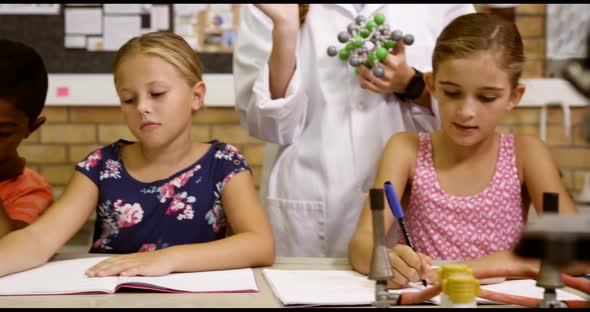 Teacher assisting school kids with molecule model in classroom