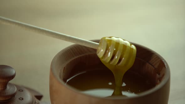 Honey with Wooden Honey Dipper in Wooden Bowl on Wooden Table