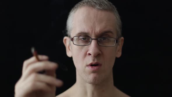 Caucasian Man in Glasses Smokes a Cigarette on a Black Background