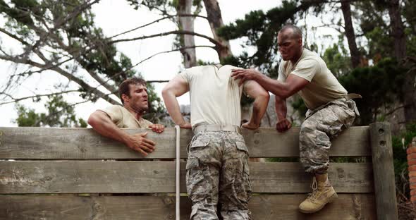 Male soldiers assisting their team mate to climb a wooden wall 