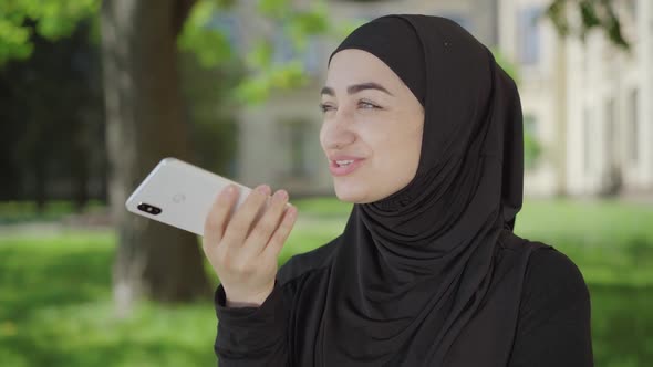 Smiling Beautiful Muslim Woman Recording Audio Message on Smartphone. Portrait of Confident Joyful