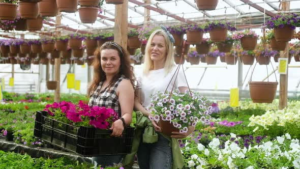 Female farmers stand between rows of flowers holding boxes  and looking camera