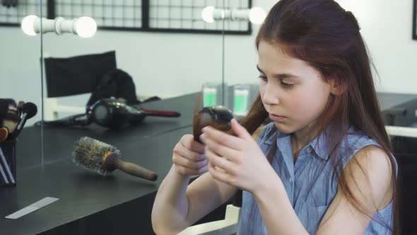 Little Cute Girl Looking Sad Examining Her Damaged Hair with Split Ends