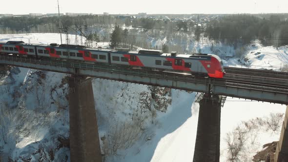 Aerial Shot Top Shot of a Train Crossing a Bridge Over the Mountain River in Sunny Winter Day