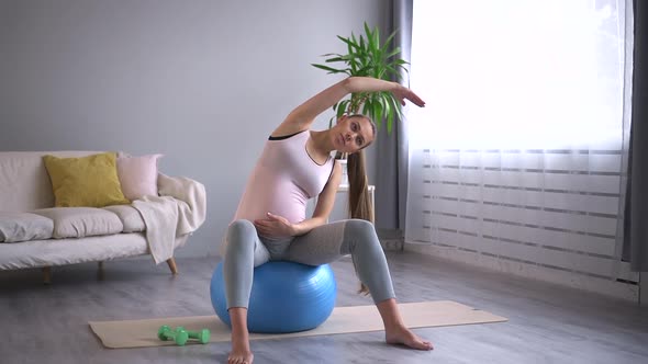 Pregnant Woman Practice Arm Stretching Exercise on Yoga Fit Ball in Apartment Room Spbd