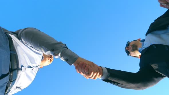 Young Salesman in Formal Suit Greeting with Male Buyer and Giving Him Keys of Car on the Blue Sky