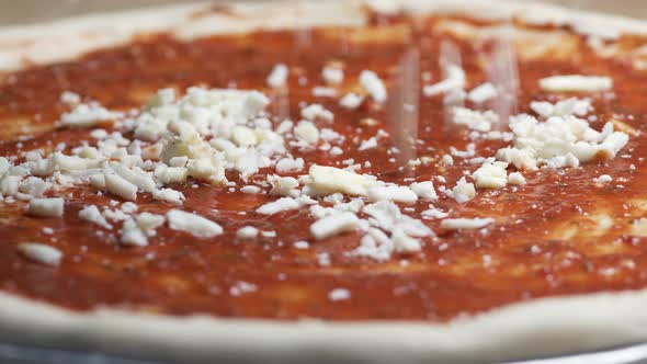 close-up of a spoon spread a juicy red tomato sauce on pizza dough.