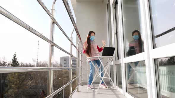 Teenager Girl in Mask and Headphones, Listening To Music on Laptop, Chatting Online, on Open Balcony